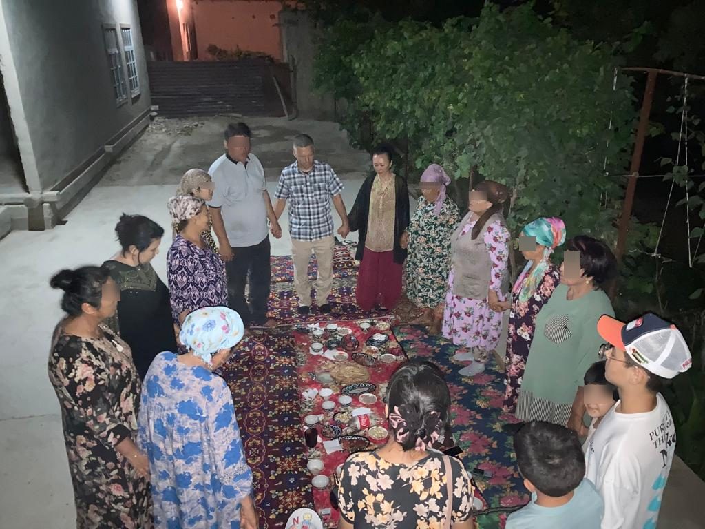 Believers standing in a circle holding hands in prayer around a shared meal